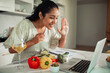 © Marko Geber - Smiling woman waving to laptop during online cooking class in home kitchen