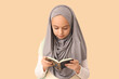 © Pixel-Shot - Little Muslim girl in hijab reading Koran on beige background