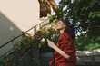 © SHOTPRIME STUDIO - A woman in a red coat stands outdoors, looking up with a phone in hand. A calm, sunny day frames a casual street style and reflective mood