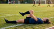 © Mukhliez - Female soccer player lying on grass field stretching her leg during team practice
