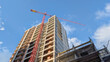 © Newleks - Building with a large red crane on a construction site, workers developing a new high rise residential or commercial complex, signifying progress and urban expansion