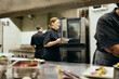 © Maskot - Busy female chef holding plate while walking in kitchen during service