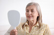 © New Africa - Senior woman looking in mirror at her teeth with dental implant at clinic