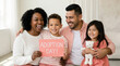 © Len_mik - Diverse family holding Adoption Day sign. Happy parents and children celebrating together with teddy bear at home