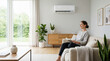 © Lina - Happy woman reading a book on a sofa under a wall mounted air conditioner. Modern living room interior with fresh indoor air quality. Climate control and comfort at home