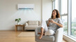 © Lina - Cheerful woman enjoying cool air from a wall mounted air conditioner at home. Happy female sitting in armchair with a mug in a modern living room. Climate control and cooling solution concept