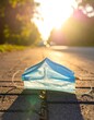 © putri - Disposable face mask left on asphalt road with warm sunlight and trees