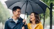 © Angavlan - Couple laughing in the rain under black umbrella with joyful expressions, wearing colorful jackets and enjoying the moment together. The cheerful scene symbolizes love and connection on rainy days.