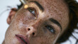 © CYBERPINK - Close-up portrait of a young woman's face. she has freckles on her face and her eyes are looking directly at the camera. her hair is styled in loose curls and she has a slight smile on her lips.