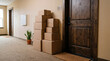 © sommersby - Stack of brown cardboard shipping boxes sitting on carpeted floor in quiet apartment hallway outside wooden apartment door, conveying move-in or delivery theme.