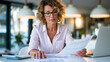 © Olha Havelia - Tax preparation concept, businesswoman in smart casual attire reviewing printed financial statements at a modern office desk, calculator and laptop open beside her, warm daylight t
