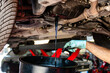 © Lorenzo Dottorini - Mechanic performing an engine oil change while used motor oil drains from the oil pan into a collection container in an automotive repair workshop