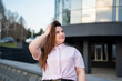© timoha.ig - Confident young professional woman in casual attire outside modern glass office building. Corporate lifestyle urban workplace and career success