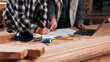 © peopleimages.com - Hands, writing and documents in lumber workshop, carpenter and team with invoice, laptop and woodwork. Workspace, collaboration and people with tech, notes and online order with carpentry planning