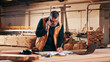 © peopleimages.com - Carpenter, phone call and man on laptop in workshop for planning, schedule or writing quote. Warehouse, mature person or carpentry with technology for woodwork or furniture production with paperwork