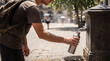 © Anastasiya - Man traveler refills reusable metal bottle at public fountain in sunny city square showing hydration break sustainable tourism heat relief outdoor lifestyle water access eco travel wellness routine