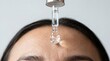 © Li - Dropper applying clear liquid serum close up onto a forehead