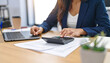 © baa - Woman in blue blazer using calculator at desk with laptop and papers, financial analysis, accounting, office work