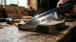 © wan - Macro shot of a hand holding a sharpened metal knife with the words FOCUS AND DRIVE engraved on the blade, cutting into a block of wood on a rustic workshop workbench.