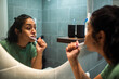© Marko Geber - Young woman brushing teeth in home bathroom mirror