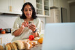 © Marko Geber - Young woman using smartphone for recipe while cooking in home kitchen