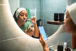 © Marko Geber - Woman brushing teeth and using smartphone in modern bathroom