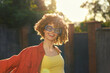 © SHOTPRIME STUDIO - A smiling young woman with curly hair in a yellow top and red jacket enjoys an outdoor sunny day, exuding carefree energy and fashion-forward confidence