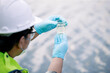 © nikomsolftwaer - Ecologist examining water sample in clear flask near waterbody wearing safety gear and gloves for environmental assessment