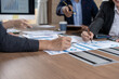 © NanSan - Business team reviewing charts and reports at a meeting table, pointing at data and discussing strategy in a modern office.