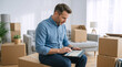 © Vyatcheslav - Man using tablet while sitting on cardboard box in new home. Male planning relocation in living room. Moving and real estate concept