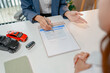 © PHOTO4U - Professional car sales consultation with a customer reviewing documents, discussing vehicle options, signing purchase agreements, and handing over car keys in a modern dealership office.