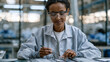 © forenna - Ethiopian woman assembles lithium battery cell modules at a manufacturing workstation, placing electrode stacks with precision tweezers, wearing anti-static wrist straps and