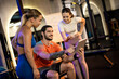 © Mediteraneo - A seated personal trainer showing a digital workout plan on a tablet to two standing women in a gym.