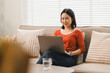 © PRIME STOCK LAB - Young woman sitting on a couch working remotely using a laptop in a bright living room