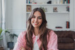 © Daniel - Young woman with long brown hair smiling confidently and looking directly at the camera, wearing a striped pink shirt in a modern home interior with bookshelves in the background