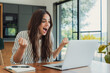 © Daniel - Young woman cheers with enthusiasm at her laptop in a bright home office, celebrating success during remote work or a video call. Natural light, casual outfit, productivity and positive emotions.