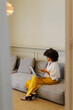 © BONNINSTUDIO/Stocksy - Woman working remotely using laptop and phone on sofa