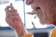 © luciano - Senior adult man with gray beard eating food from a spoon, consuming a healthy and balanced meal for proper nutrition and overall wellbeing