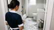 © Olga Ко - Messy hotel bathroom with used towels dropped on the floor. Over the shoulder view of a maid in uniform. Housekeeping concept.