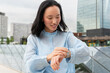 © ADDICTIVE STOCK - Gen Z Asian woman checking smartwatch in modern city