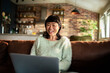 © Davor - Smiling woman video chatting on laptop at home
