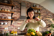 © Davor - Smiling woman photographing fresh vegetables in home kitchen