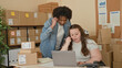 © Krakenimages.com - Woman using laptop while man points to screen amid stacked boxes in a warehouse building; teamwork focused.