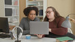 © Krakenimages.com - Woman holding laptop and pointing at screen inside an office building with bookshelves and lamp; teamwork focus.