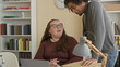 © Krakenimages.com - Woman typing on laptop while man leans over and rests hand on a stack of folders at desk in a building office with lamp and bookshelf visible; supportive collaboration.