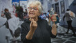 © Krakenimages.com - Senior woman shows middle finger while holding a water bottle on a cobblestone street; playful defiance.