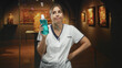 © Krakenimages.com - Woman nurse in white coat holding a blue bottle, hand on hip, standing amid framed paintings in a dim gallery building; wry resignation.