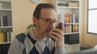© Krakenimages.com - Man holds smartphone to mouth while speaking near desk and computer in a building office with bookshelves and plant; concern focus patience.