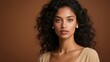 © YuanGeng - Portrait of a woman with curly dark hair wearing pearl earrings and a beige top against a warm brown background