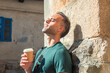 © tetxu - Time for a break! Relaxed young man drinking coffee while leaning against a stone wall in the street